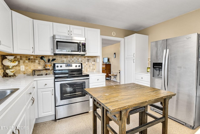 kitchen with white cabinets, tile counters, stainless steel appliances, light floors, and decorative backsplash