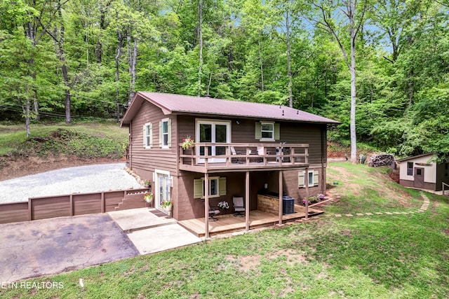 back of property with a yard, a view of trees, a wooden deck, and metal roof