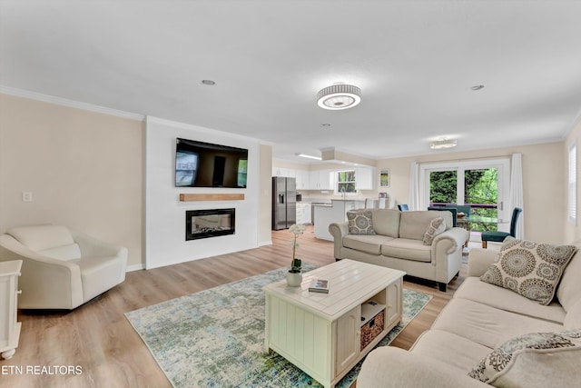 living room featuring ornamental molding, a glass covered fireplace, baseboards, and light wood-style floors