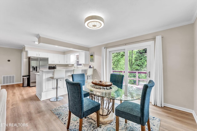 dining room featuring baseboards, visible vents, ornamental molding, and light wood-style flooring