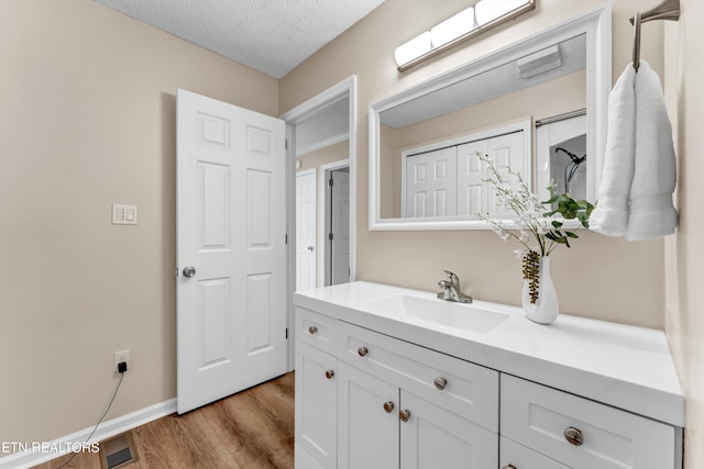 bathroom with a textured ceiling, visible vents, baseboards, wood finished floors, and vanity
