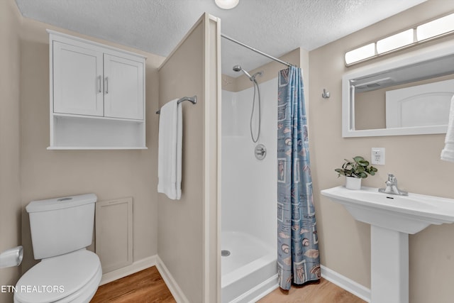 full bath featuring a shower stall, toilet, baseboards, a textured ceiling, and wood finished floors