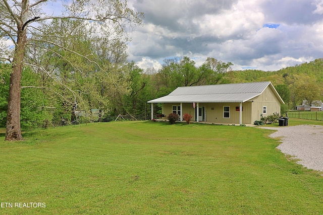 view of front of house with a porch, a wooded view, metal roof, driveway, and a front lawn