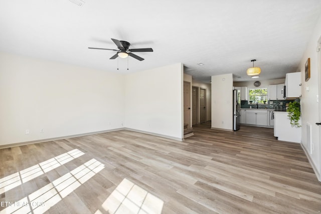 unfurnished living room with baseboards, a ceiling fan, and light wood-style flooring