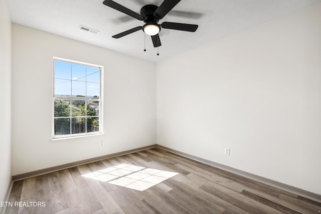 spare room with wood finished floors, visible vents, baseboards, and ceiling fan