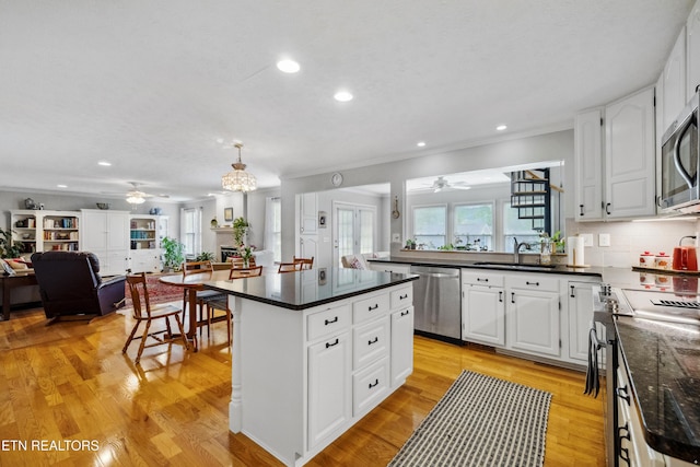 kitchen with a sink, appliances with stainless steel finishes, dark countertops, open floor plan, and a ceiling fan