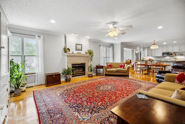living room with ornamental molding, a tiled fireplace, recessed lighting, and light wood-style flooring
