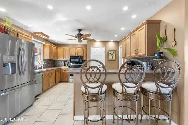 kitchen featuring tasteful backsplash, a peninsula, appliances with stainless steel finishes, and a sink