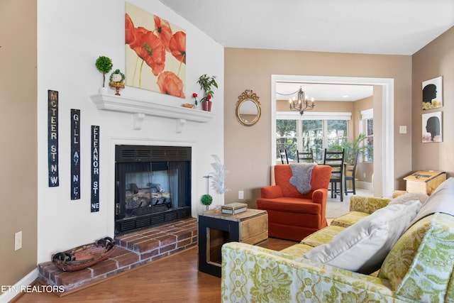 living area featuring a brick fireplace, an inviting chandelier, and wood finished floors
