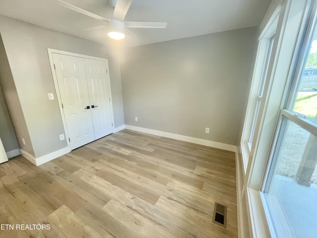 unfurnished bedroom featuring light wood-style flooring, a closet, baseboards, visible vents, and a ceiling fan
