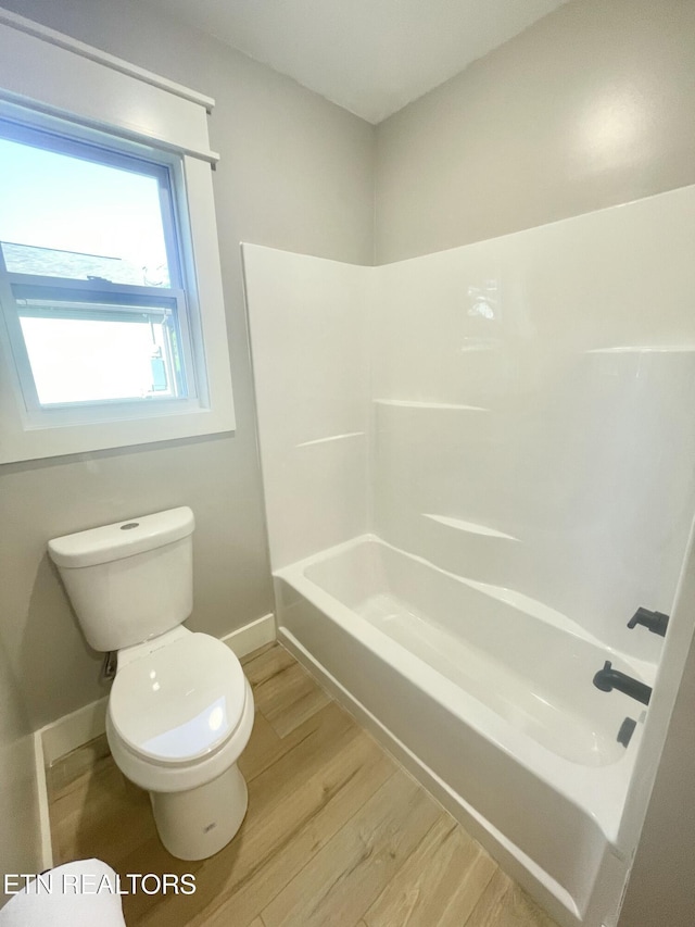 bathroom with baseboards, wood finished floors, toilet, and shower / bathtub combination