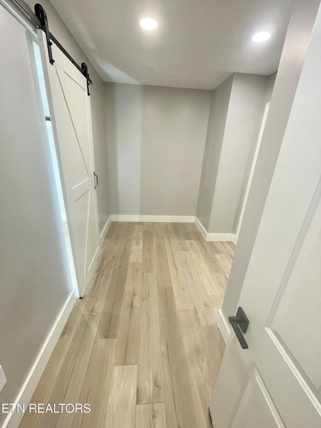 basement with recessed lighting, baseboards, a barn door, and light wood-style floors
