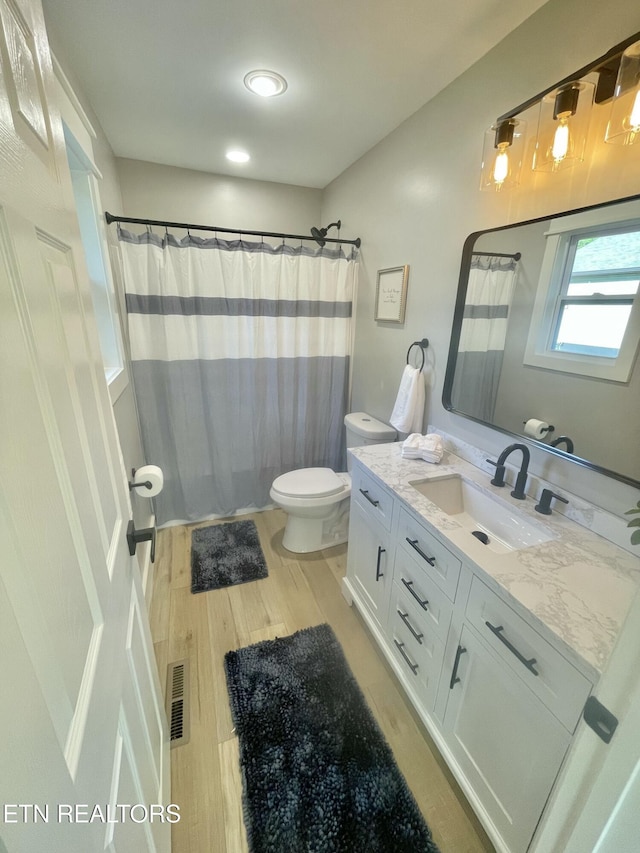 bathroom with a shower with curtain, visible vents, toilet, wood finished floors, and vanity