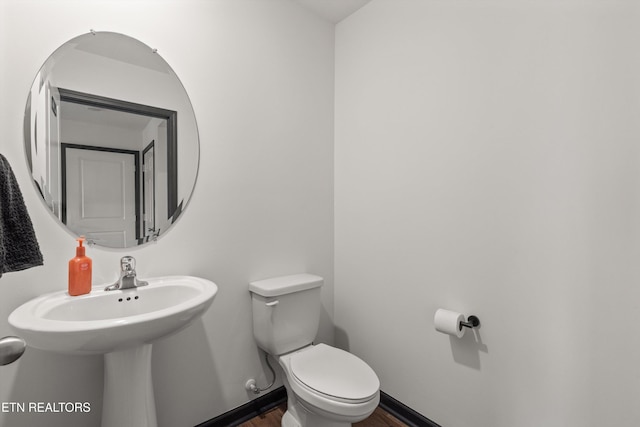 half bath featuring baseboards, wood finished floors, and toilet