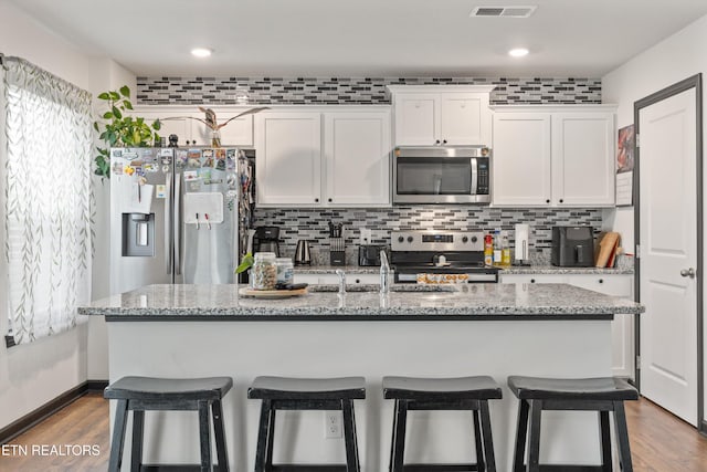 kitchen with stainless steel appliances, white cabinetry, a kitchen breakfast bar, and tasteful backsplash