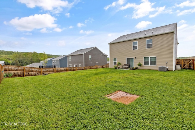 rear view of property with a yard, central AC, and a fenced backyard