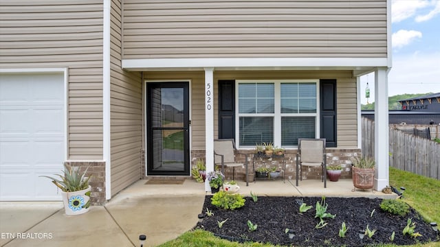view of exterior entry featuring fence, an attached garage, a porch, and brick siding
