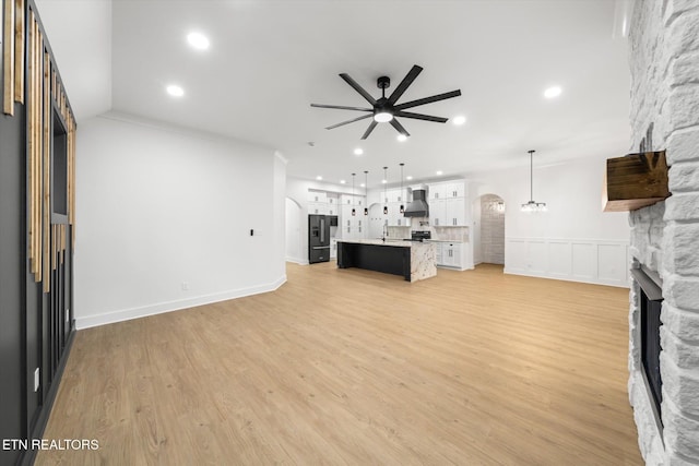 unfurnished living room with light wood-style floors, a fireplace, arched walkways, a ceiling fan, and recessed lighting