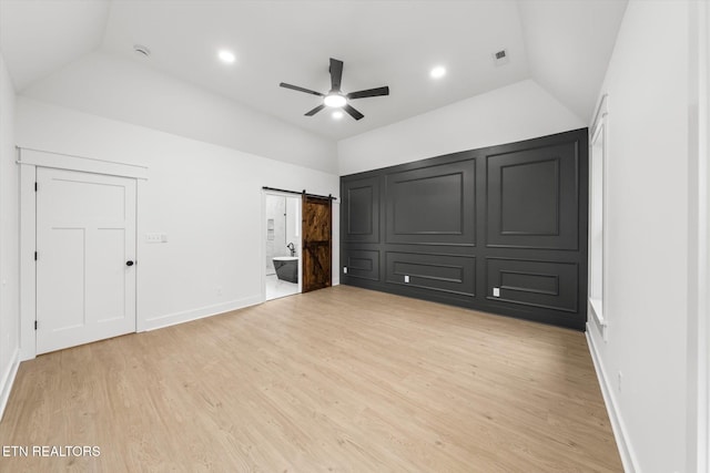 unfurnished bedroom featuring vaulted ceiling, light wood-type flooring, a barn door, and visible vents