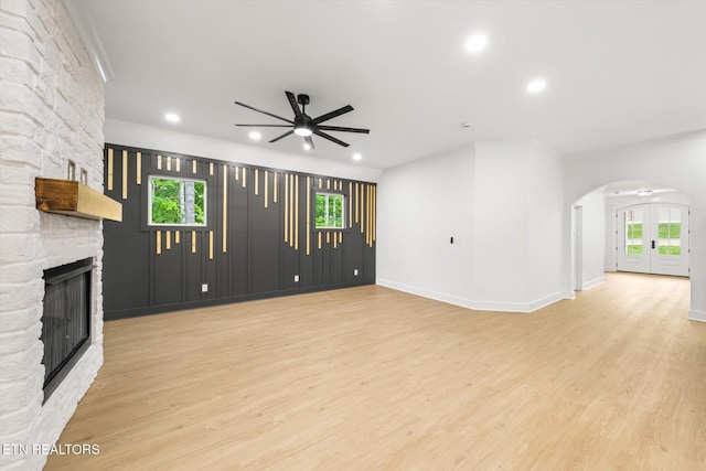 unfurnished living room with arched walkways, ceiling fan, a stone fireplace, and wood finished floors