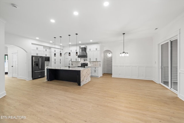 kitchen featuring a sink, arched walkways, recessed lighting, a center island with sink, and black appliances