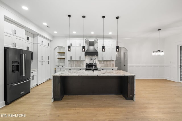 kitchen with arched walkways, tasteful backsplash, a sink, black appliances, and wall chimney exhaust hood