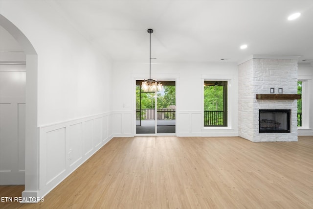 unfurnished living room with a wainscoted wall, a stone fireplace, wood finished floors, and a decorative wall
