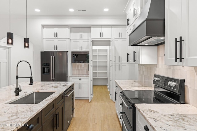 kitchen with white cabinets, a sink, light wood-style flooring, stainless steel appliances, and custom range hood