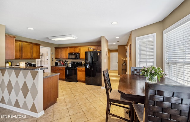 kitchen with brown cabinetry, light tile patterned floors, baseboards, black appliances, and a peninsula