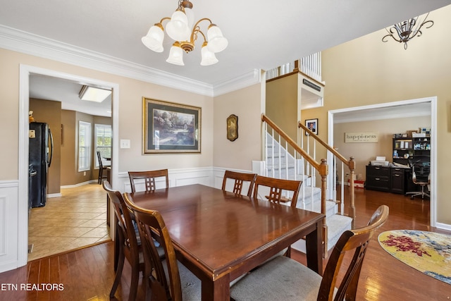 dining room featuring crown molding, wainscoting, wood finished floors, a notable chandelier, and stairs