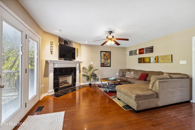 living room with visible vents, wood finished floors, baseboards, ceiling fan, and a tile fireplace