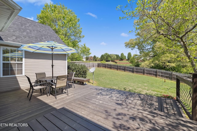 wooden terrace featuring outdoor dining area, a fenced backyard, and a yard