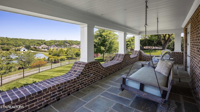view of patio with fence, covered porch, and a water view