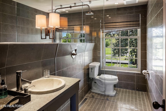 bathroom with tile walls, tiled shower, vanity, tile patterned floors, and toilet