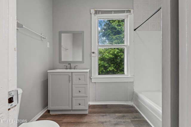 bathroom featuring a shower, baseboards, toilet, wood finished floors, and vanity