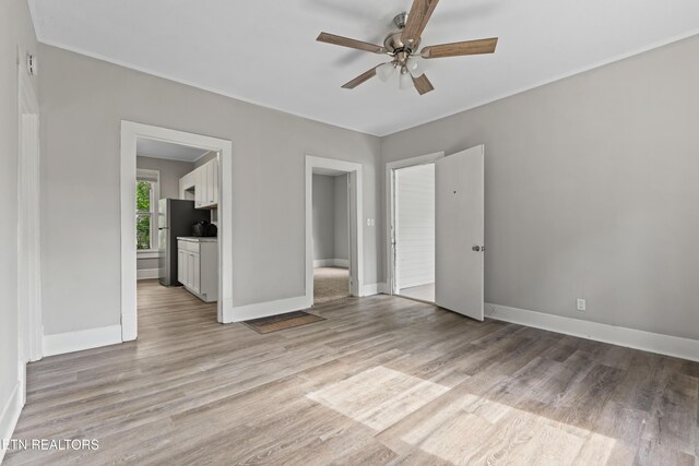 unfurnished bedroom with connected bathroom, light wood finished floors, freestanding refrigerator, and baseboards