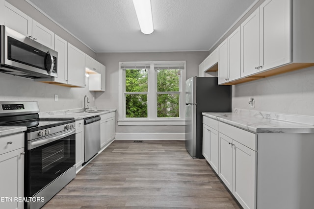 kitchen featuring a sink, light wood-style floors, a textured ceiling, white cabinets, and appliances with stainless steel finishes