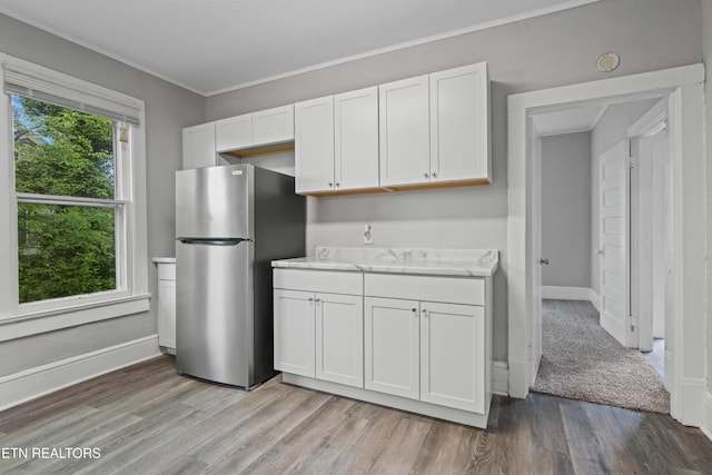 kitchen with light wood-type flooring, baseboards, freestanding refrigerator, and white cabinetry