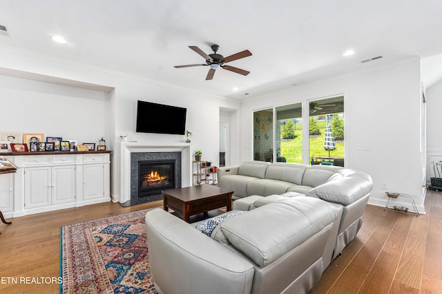 living room featuring ceiling fan, wood finished floors, a high end fireplace, visible vents, and ornamental molding
