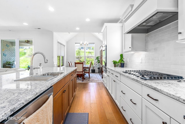 kitchen with light stone countertops, brown cabinets, custom range hood, a sink, and stainless steel appliances