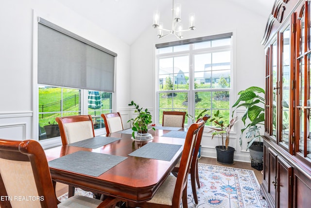 dining room featuring a chandelier, vaulted ceiling, a wainscoted wall, and a decorative wall