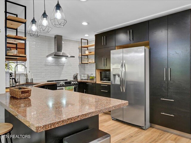 kitchen featuring a sink, dark cabinets, stainless steel appliances, light wood-type flooring, and wall chimney exhaust hood