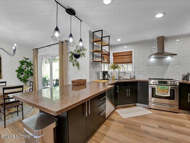 kitchen with a sink, stainless steel appliances, a healthy amount of sunlight, a peninsula, and wall chimney range hood