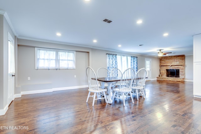 dining area with visible vents, ceiling fan, a stone fireplace, and crown molding