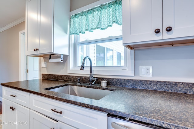 kitchen with dark stone countertops, stainless steel dishwasher, white cabinets, a sink, and ornamental molding