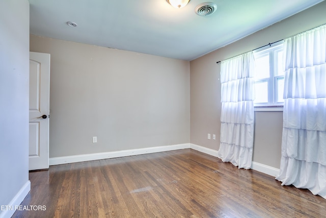 spare room featuring baseboards, visible vents, and wood finished floors