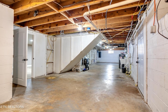 unfinished below grade area with concrete block wall, electric panel, and water heater