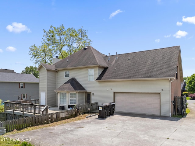 back of property with an attached garage, a shingled roof, fence, and driveway