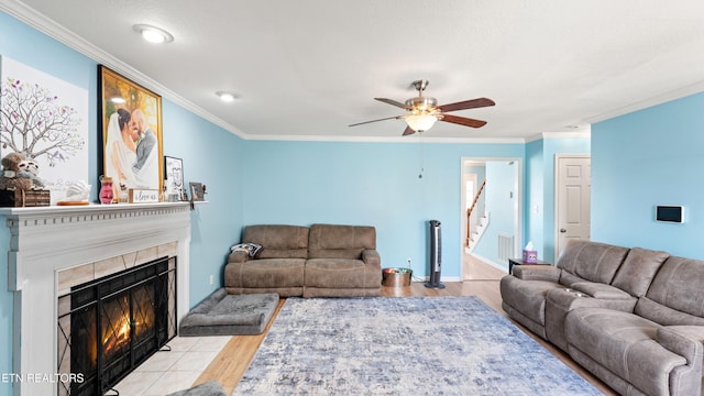 living room featuring ceiling fan, crown molding, wood finished floors, a tile fireplace, and stairs