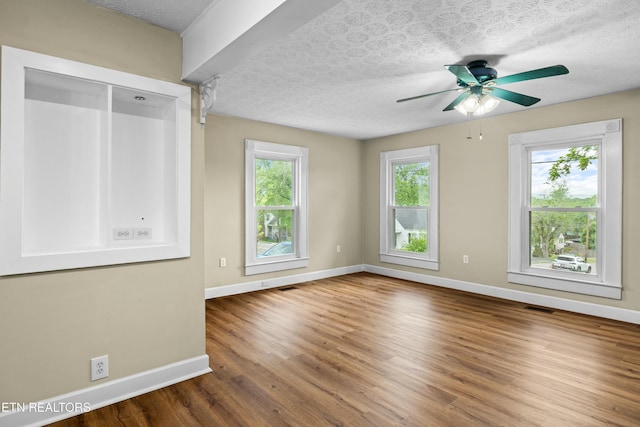 spare room featuring ceiling fan, visible vents, baseboards, a textured ceiling, and wood finished floors